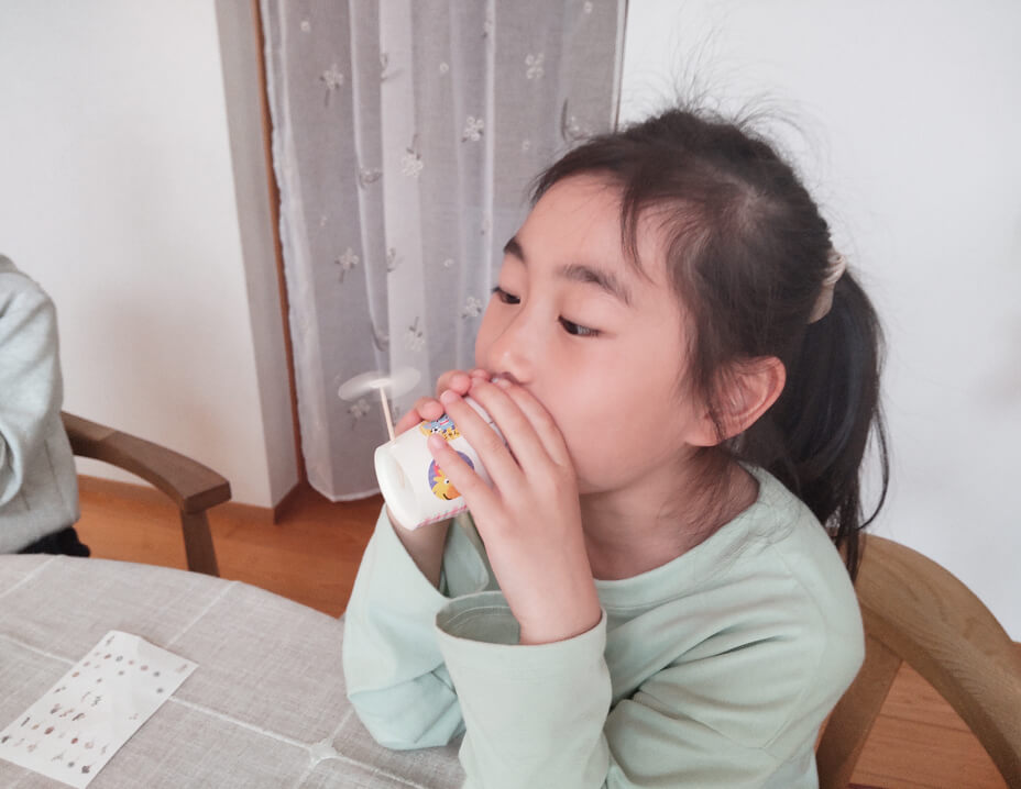 紙コップで作った楽器を吹いて遊ぶ女の子